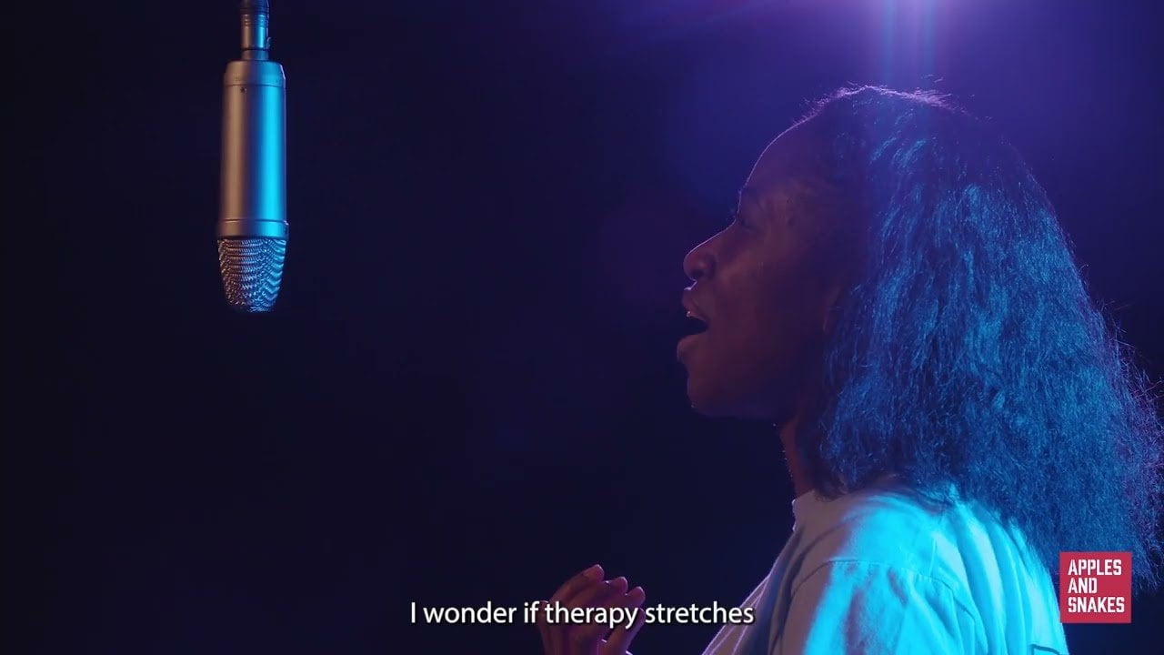 Screenshot from a video of Anneliese speaking into a microphone in a dark room with blue lighting