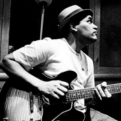 A man in a wide brimmed hat playing guitar on stage