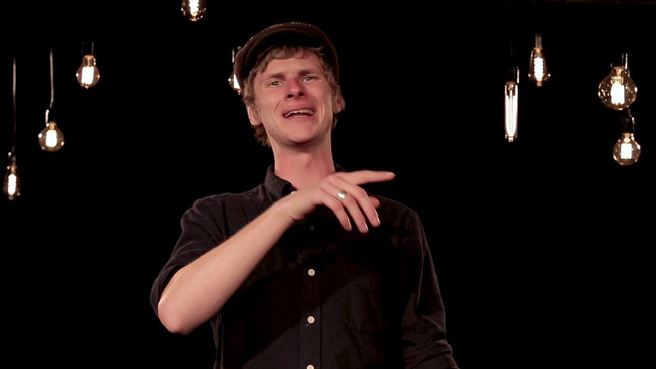 Image of a man wearing a flat cap and a black shirt in a room with hanging lightbulbs
