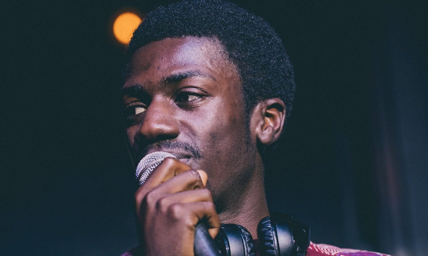 Man with tight curls speaking into a microphone