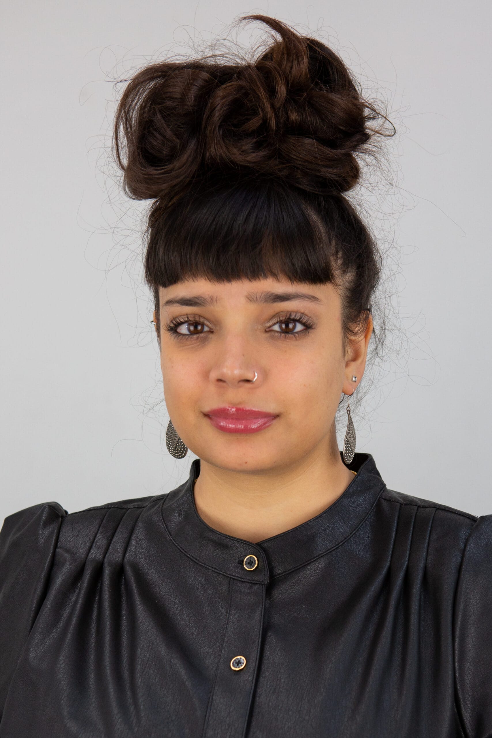 An image of poet Shareefa Energy, she wears a black top and has tear drop shape earrings. She smiles at the camera and looks directly out. She has long black hair that is tied up into a large bun on top of her head.