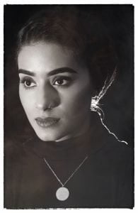 A striking woman with dark hair pulled into a hijab, nose piercing and dark features.