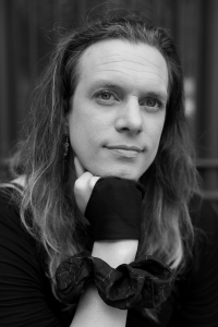 Edalia holds her chin on her hand wearing her hair long, a scrunchie around the wrist and fingerless gloves.