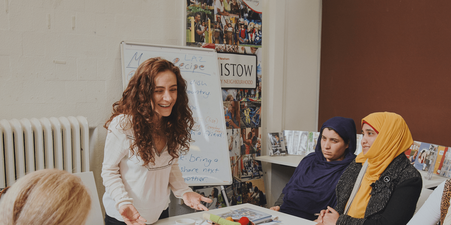 A woman with curly hair laughs. She is joined by two women in headscarves looking towards her