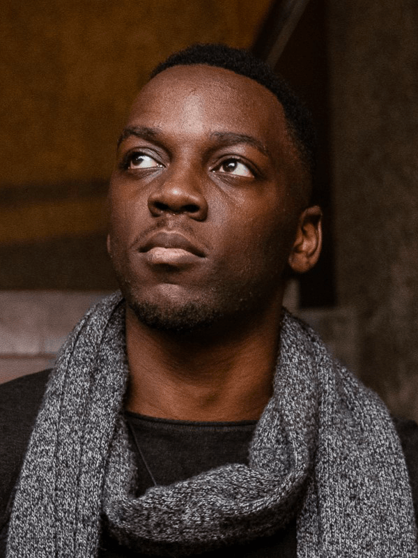 Francis has short dark hair, wearing a grey marl scarf and black top