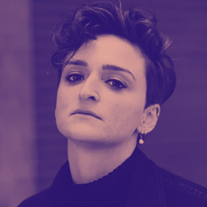 A woman with short curled hair, dangling pearl earring and black turtle neck jumper