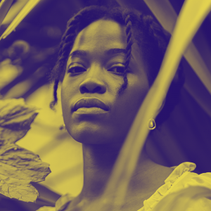 A woman with braided hair stands behind some leafy greens