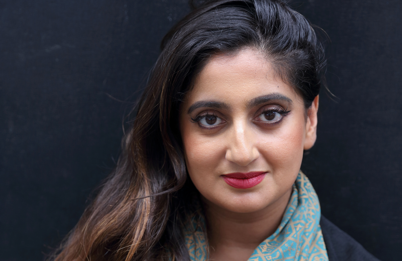 A woman with red lips and dark hair looks straight on