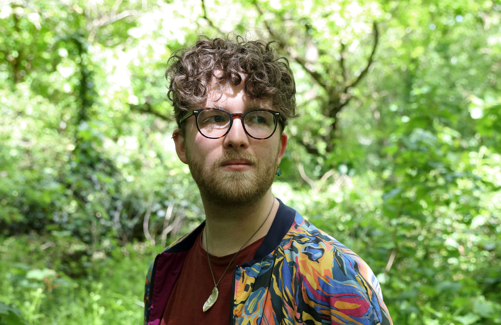 Image of Tom - a man with curly hair and glasses looking to the side