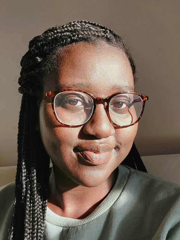 Triumph wearing her braided hair pulled into a half up style, glasses and sage green jumper